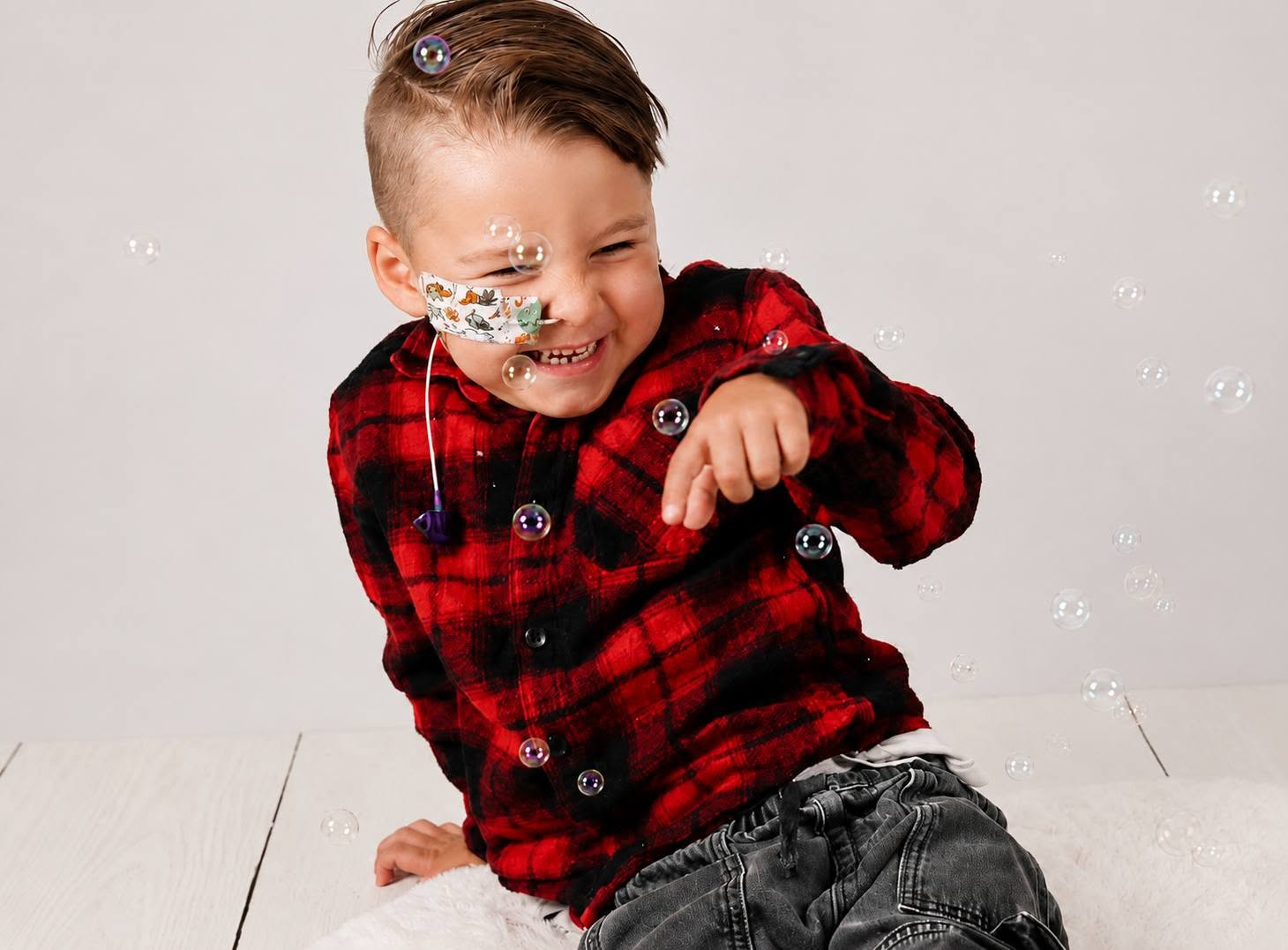 Archie George smiling and playing with bubbles, wearing a red checked shirt.